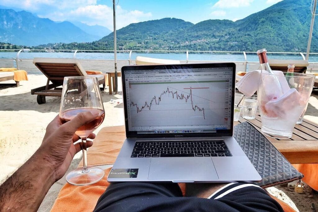 homem sentado na beira da praia com taça de vinho e com notebook no colo sonho realizado