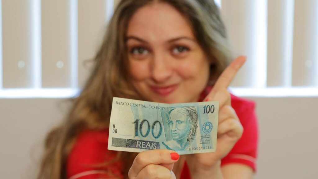 imagem de mulher sorrindo segurando uma nota de cem reais para fazer seu primeiro investimento com MEI