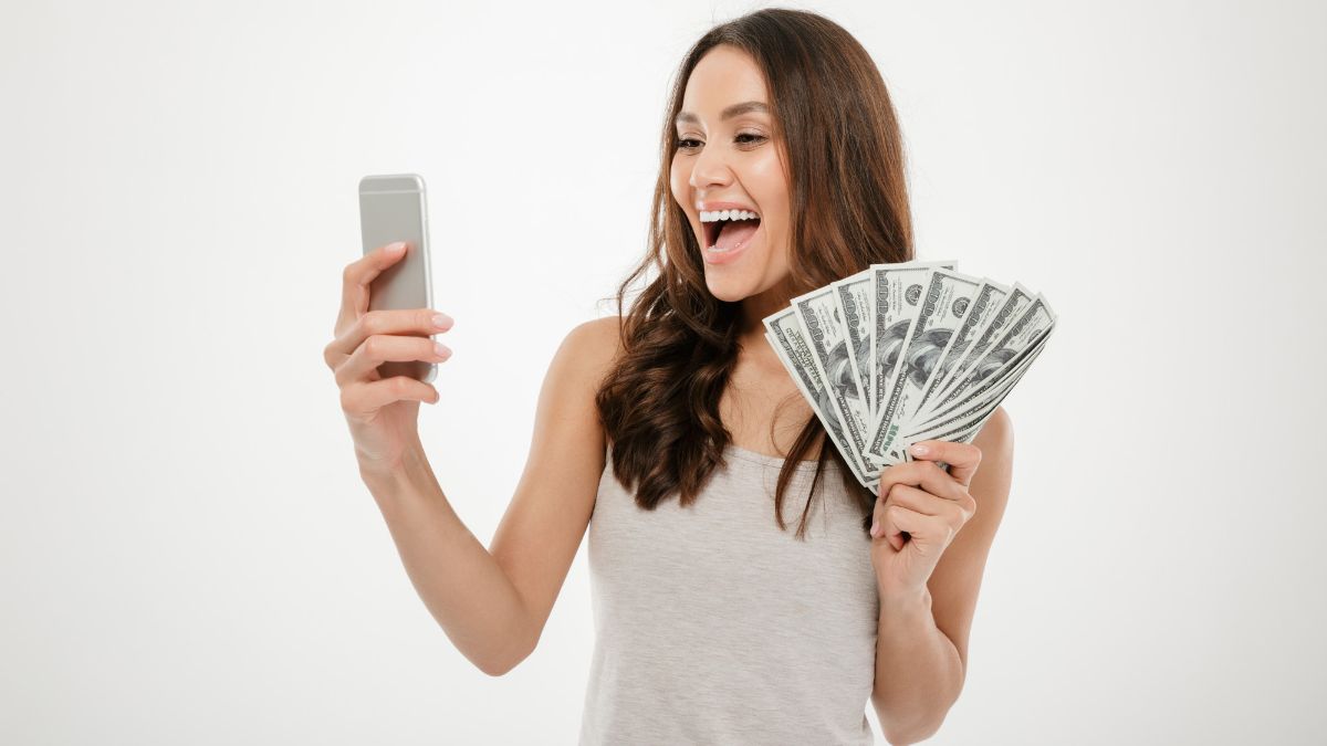 mulher segurando celular com uma mão e dinheiro com a outra mão